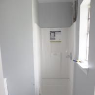 A white shower unit with a built-in shelf sits in a bathroom with gray walls and a small window on the right.