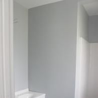 A grey wall in a corner of a bathroom next to a white sink and shower unit.