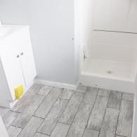 A bathroom with a white vanity, a white shower stall, and gray wood-look floor tiles.