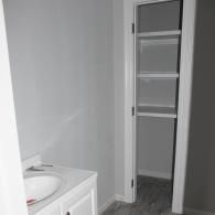 A bathroom vanity with a white sink next to a doorway leading to a small closet with white shelving.