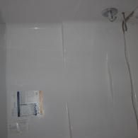 White shower wall panels with a partially peeled protective plastic film and a showerhead fixture attached at the top.