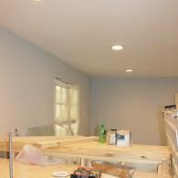 A room interior with light-colored walls, two ceiling lights, and construction materials placed on a wooden work surface.