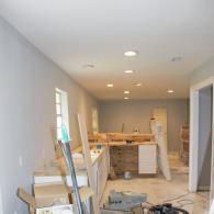 An interior room under construction with light grey walls, recessed ceiling lights, and wooden cabinets in the background.