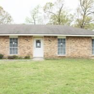 A single-story brick building with a centered white door and symmetrically placed windows under a gray roof.