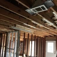 Exposed wooden ceiling joists and metal framing in a room under construction, with an HVAC vent visible overhead.