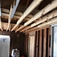 Exposed wooden ceiling joists and wall studs in a room under construction, with a white cabinet on the left.