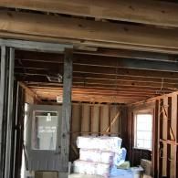 A view of a room under construction, with exposed wooden framing, a grey doorway, and wrapped insulation in the center.