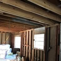 A room under construction with exposed wooden wall studs, ceiling joists, and two windows.