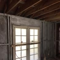 A pair of French doors set in a wall with exposed metal studs, with a wooden board braced across the front during renovation.