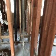 Wooden wall studs and a black pipe in an unfinished, under-construction room with concrete flooring.