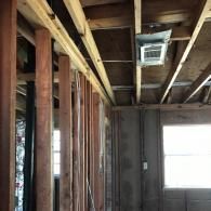 An unfinished interior room with exposed wooden wall studs, floor joists, a ceiling air vent, and a window.