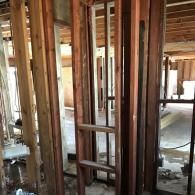 Wooden wall studs framing an interior space under construction, showing open framing against a concrete floor.