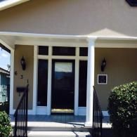 A front entrance to a house with a dark door, glass panels, a white pillar, black railing, and the house number 631.