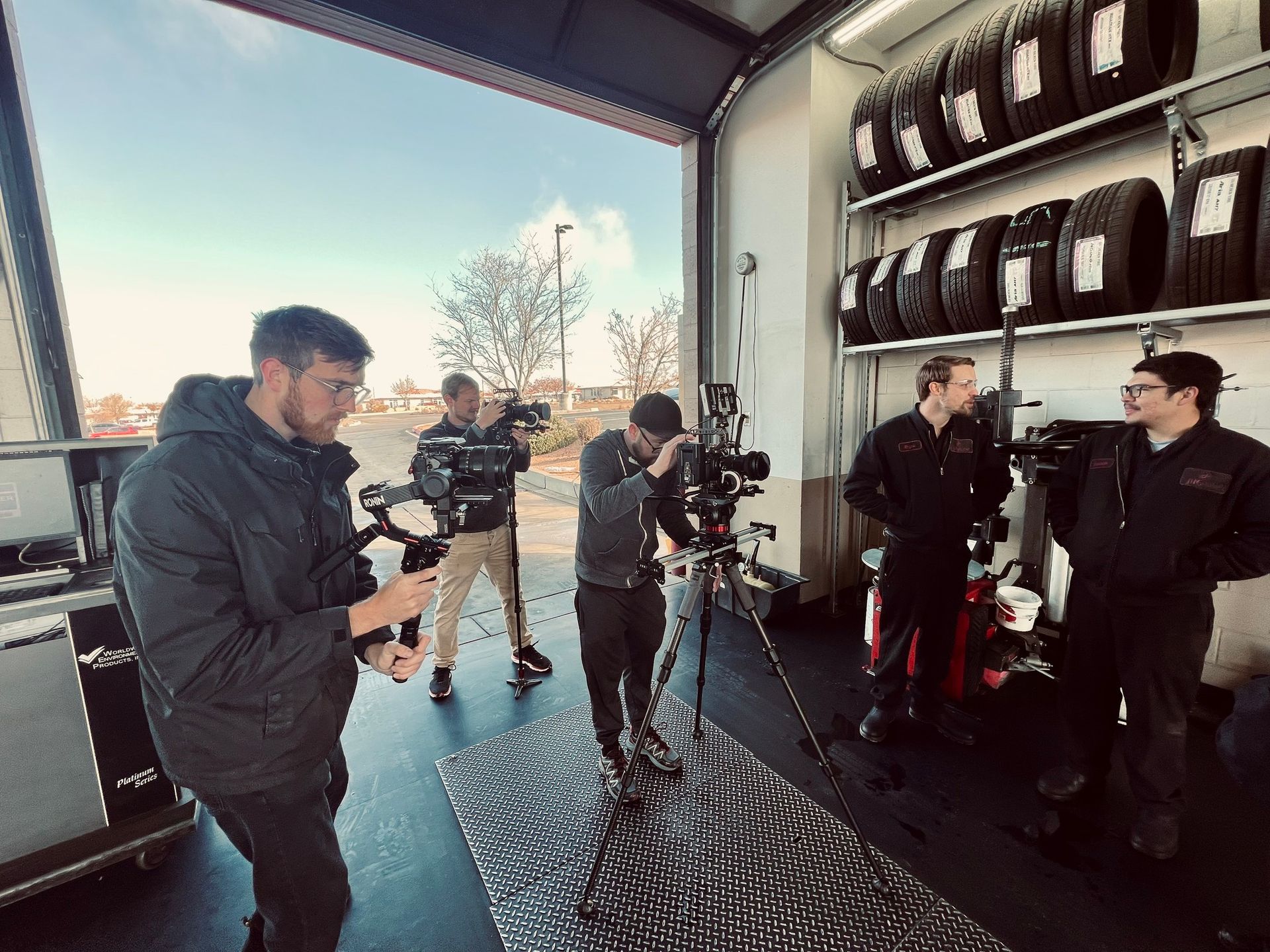 People filming indoors in a garage, with cameras, tripods, and stacked tires along the wall