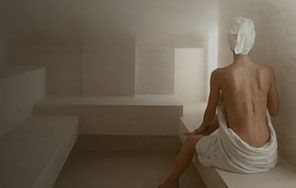 Una mujer envuelta en una toalla está sentada en una sala de vapor.