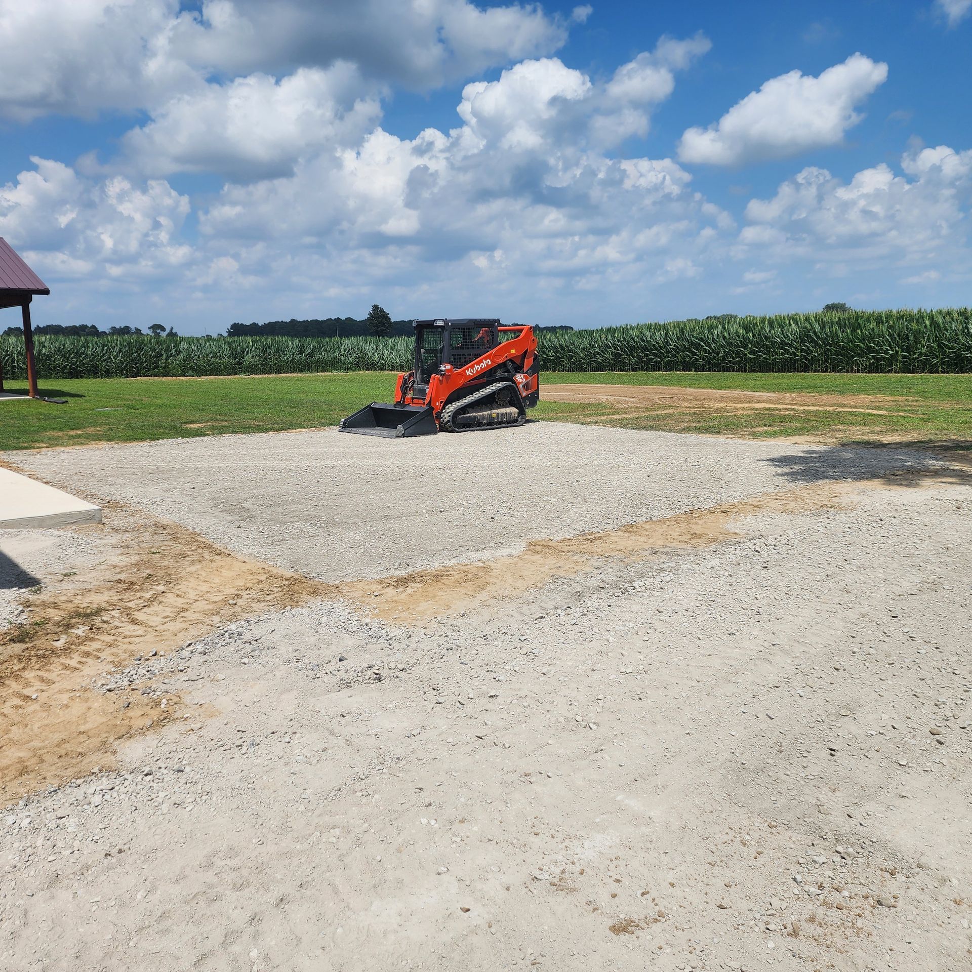 Orange skid steer on a gravel pad, preparing the ground for a project in a field on a sunny day.
