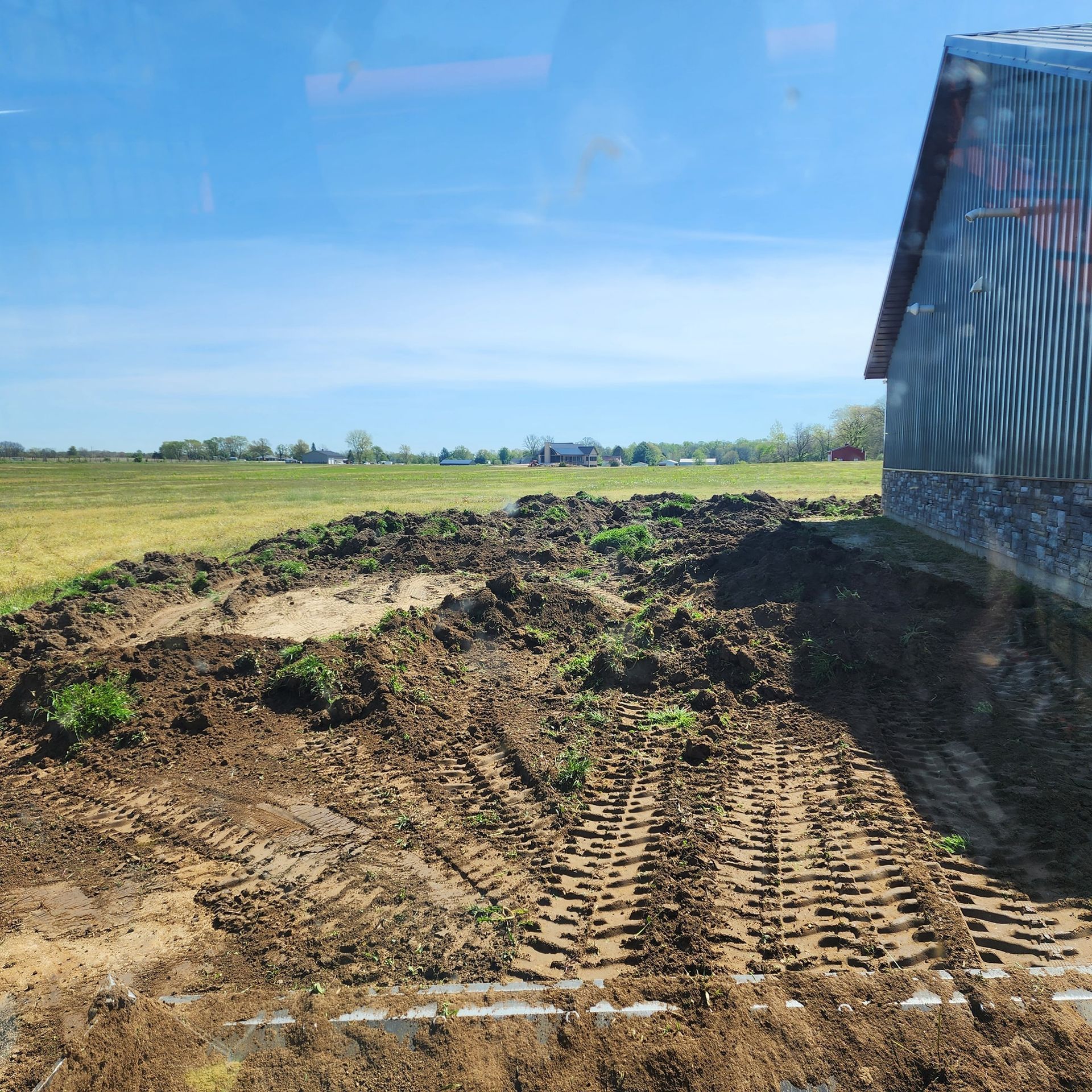 A dirt field with tire tracks, a barn, and a clear blue sky.
