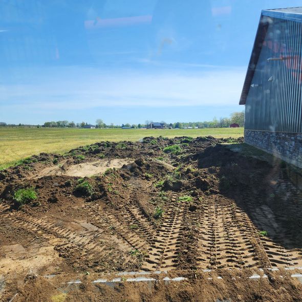 A dirt field with tire tracks, a barn, and a clear blue sky.