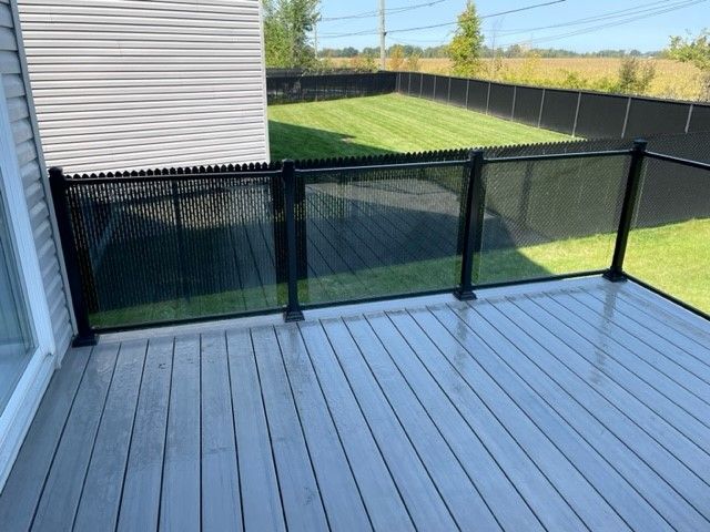 Une terrasse avec une balustrade en verre et une clôture en arrière-plan.