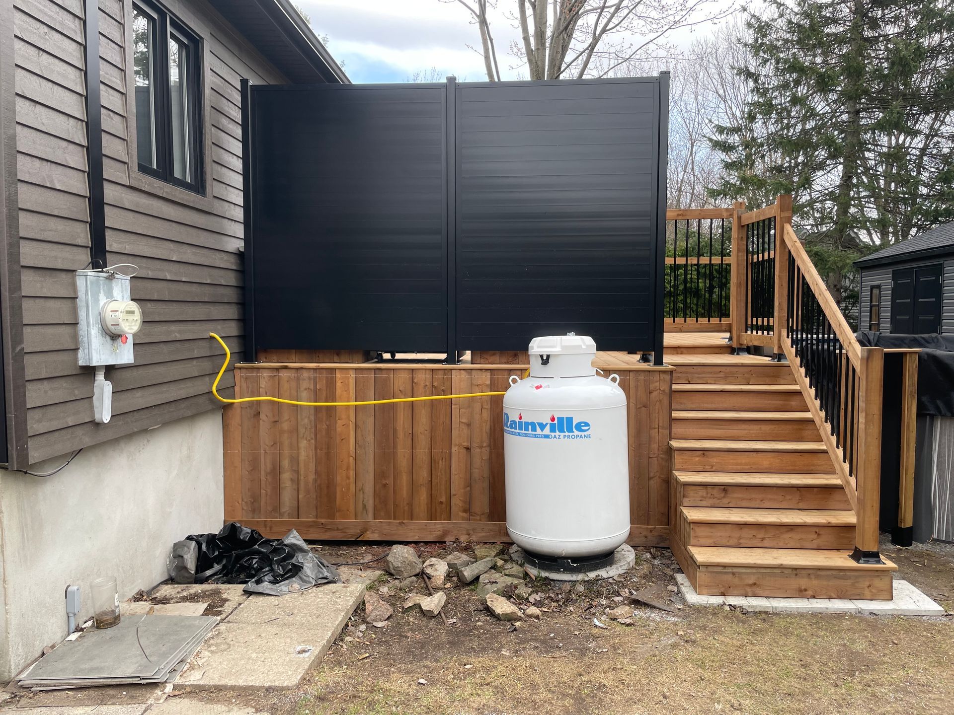 Un réservoir de propane se trouve sur le côté d'une terrasse en bois à côté d'une maison.