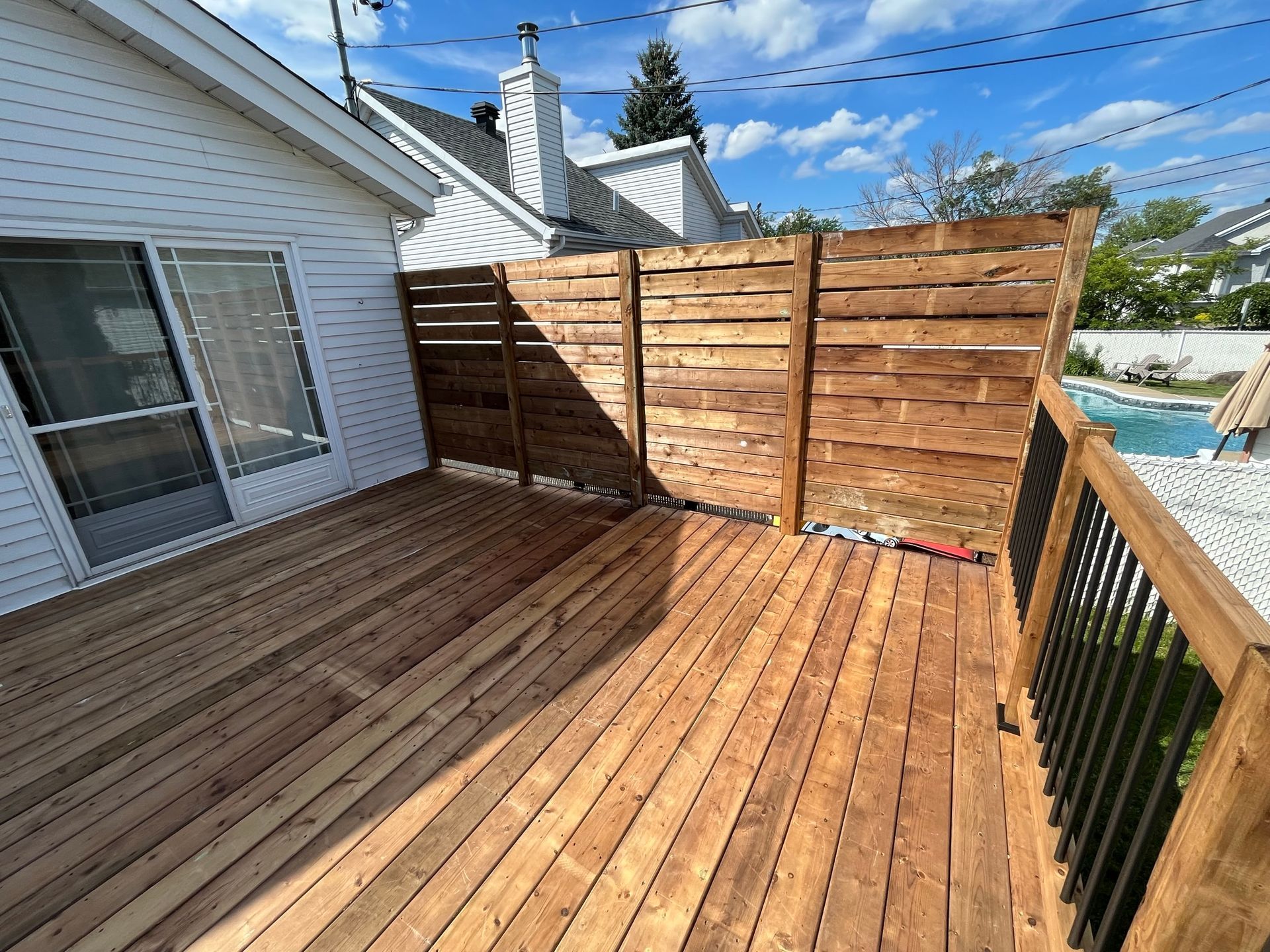 Une terrasse en bois avec une clôture et une piscine en arrière-plan.