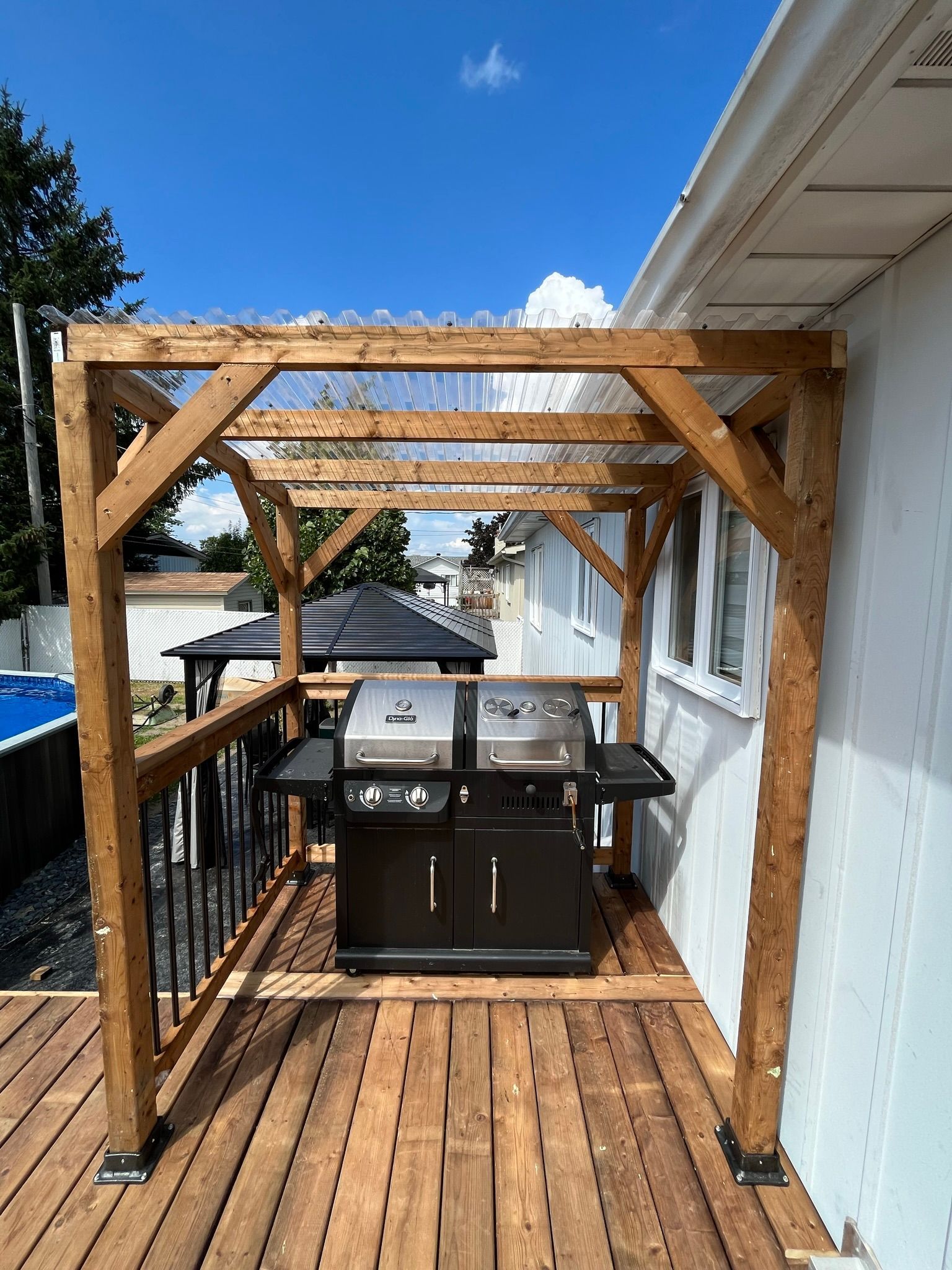 Une terrasse en bois avec grill sous pergola.