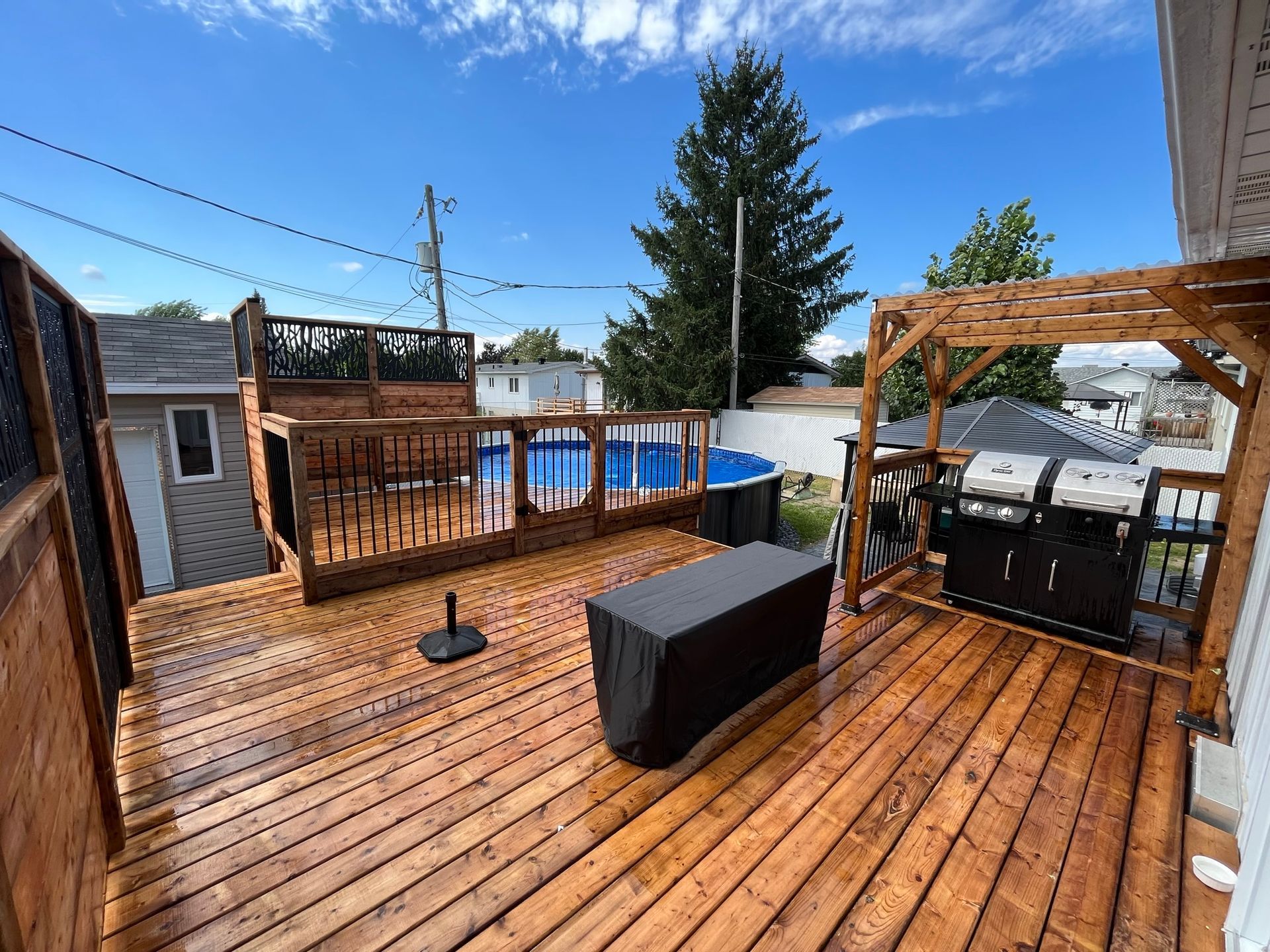 Une terrasse en bois avec un grill et une piscine en arrière-plan.