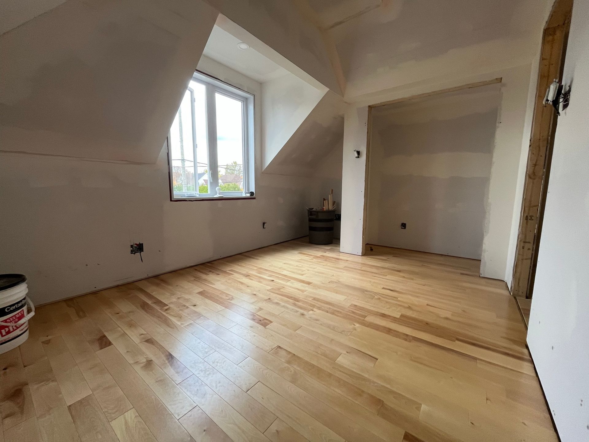 Une pièce avec parquet et fenêtre dans une maison en construction.