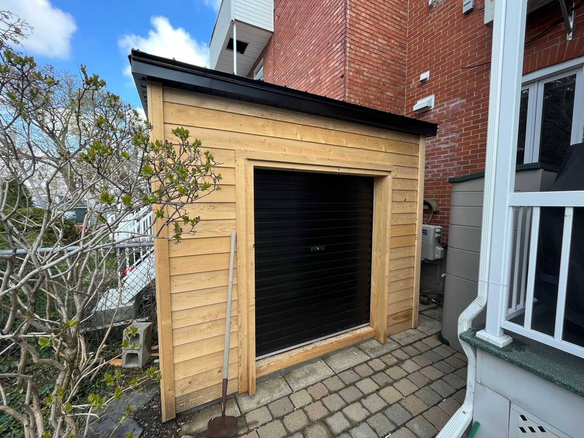Un garage en bois avec une porte noire se trouve à côté d'un bâtiment en brique.