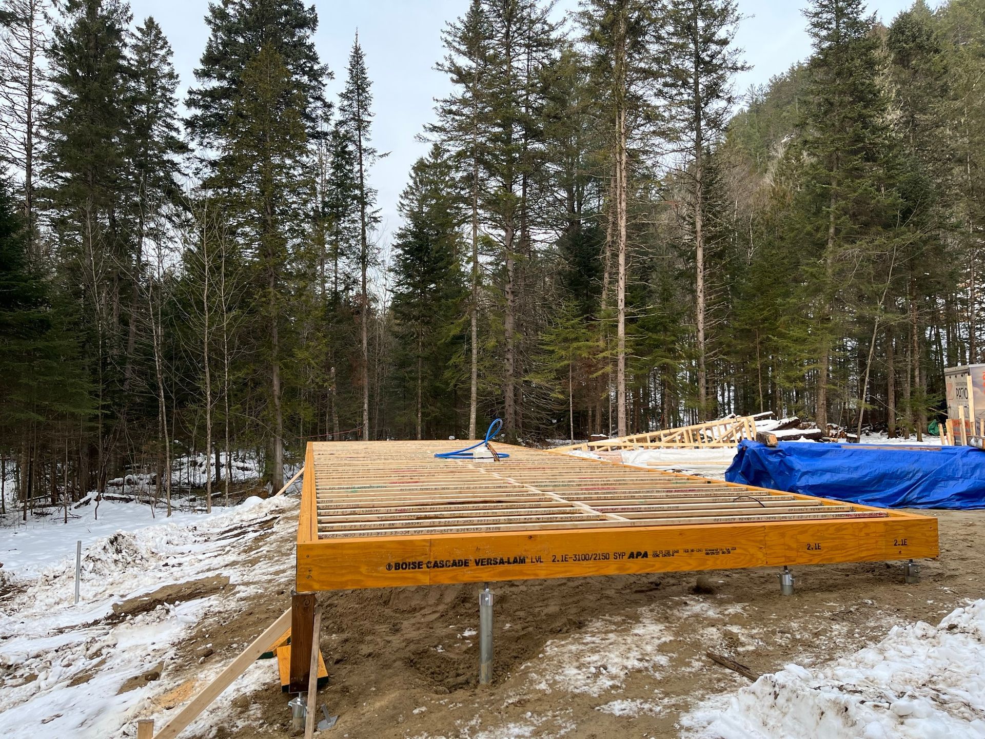 Une structure en bois est en construction au milieu d'une forêt enneigée.