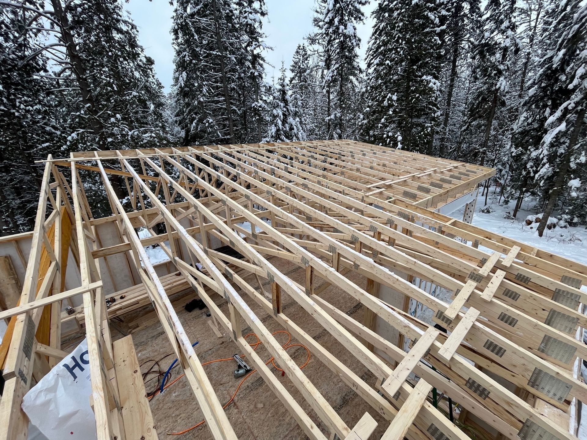 Une grande structure en bois est en construction au milieu d'une forêt enneigée.