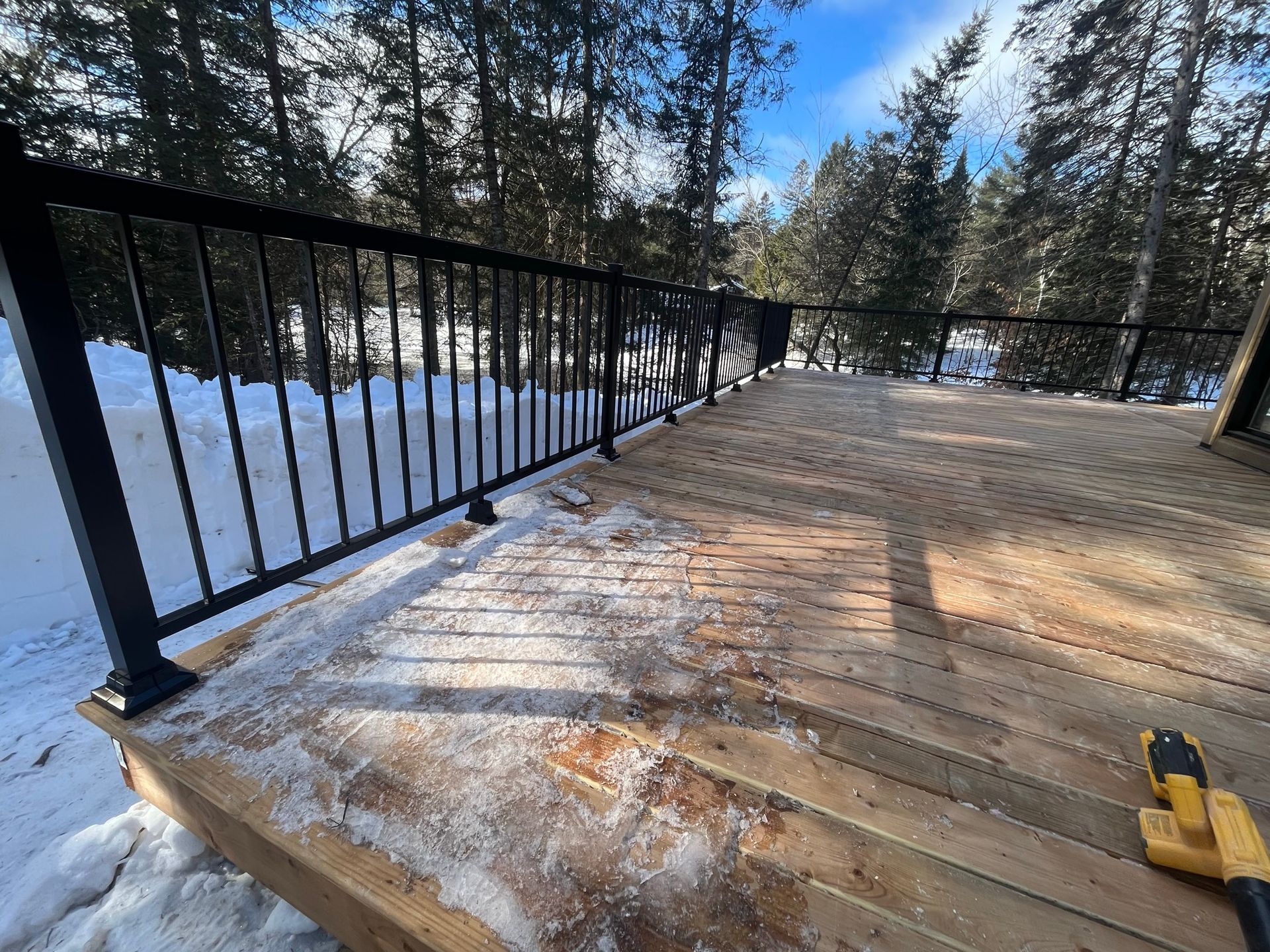 Une terrasse en bois avec une balustrade en métal dans la neige.