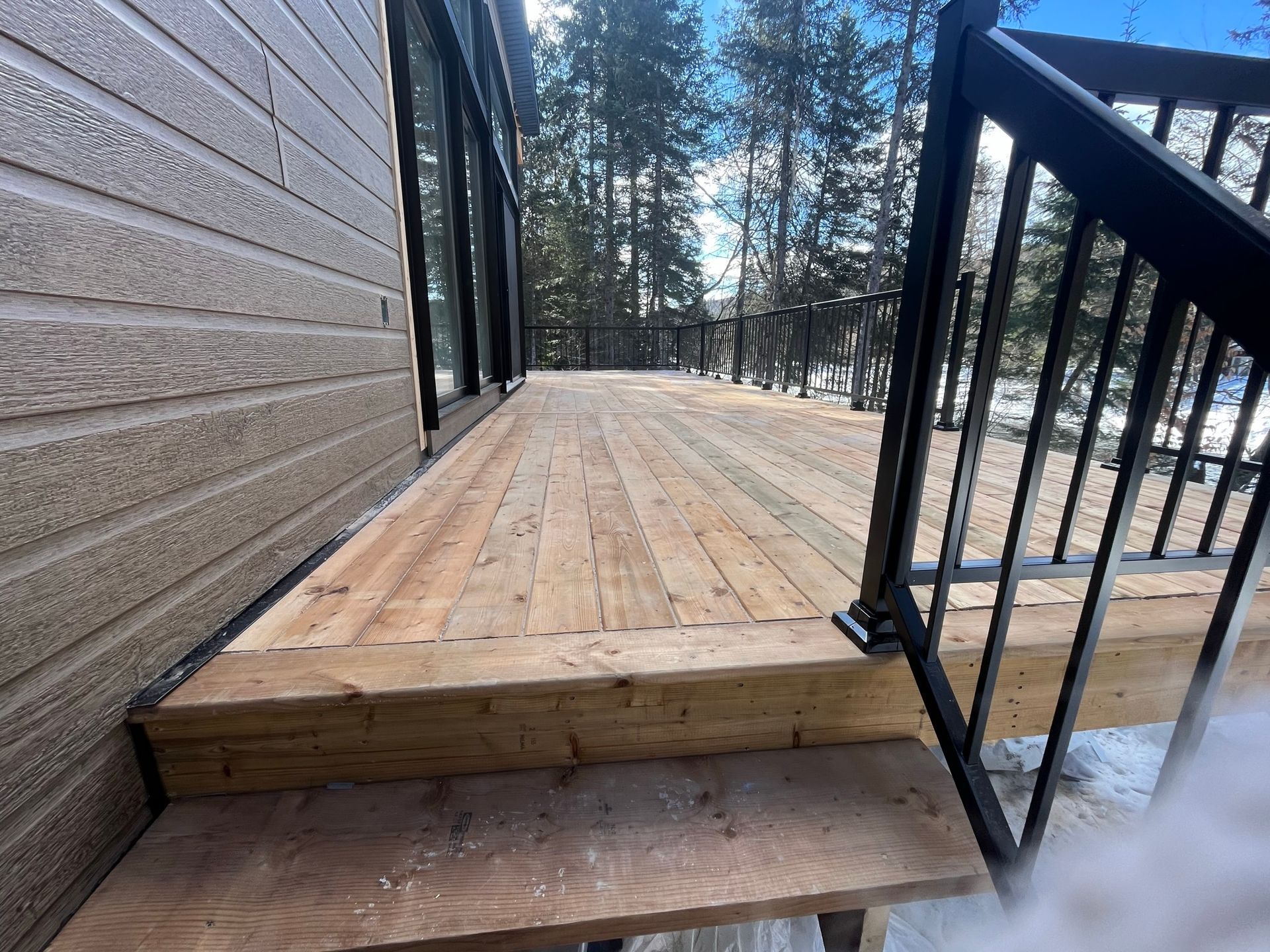 Une terrasse en bois avec des escaliers qui y mènent et une balustrade noire.