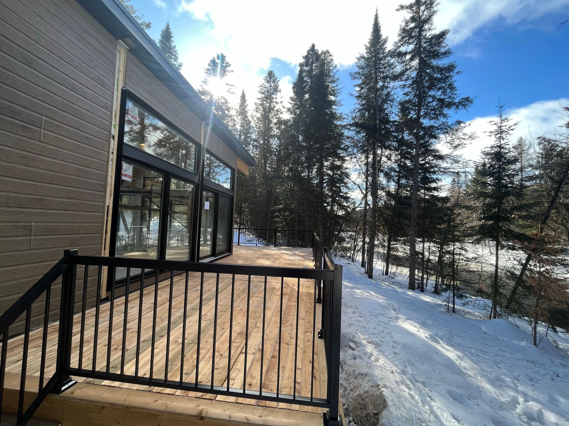 Une terrasse en bois avec une balustrade en métal est entourée d'arbres enneigés