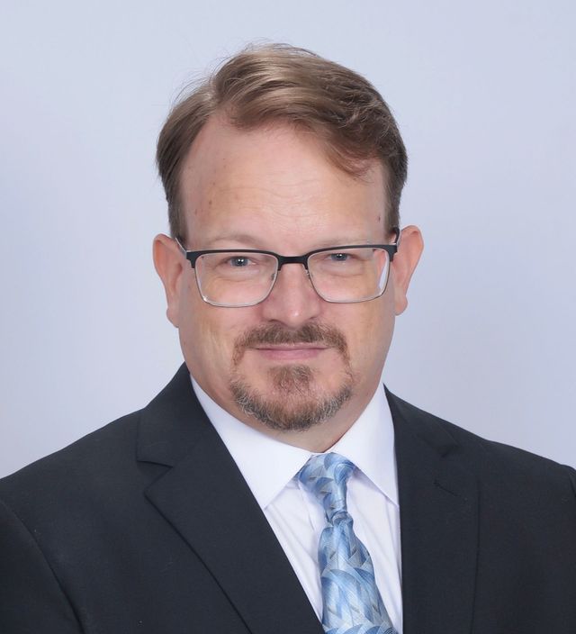 Kirt Christiansen with glasses and a beard is wearing a suit and tie.