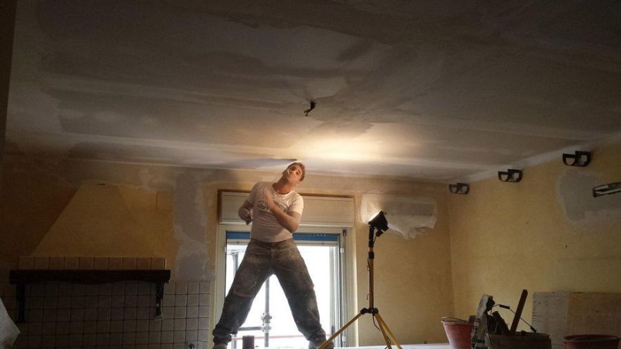 Persona in una stanza, con le braccia alzate vicino a una luce intensa. Soffitto e pareti mostrano lavori di ristrutturazione.