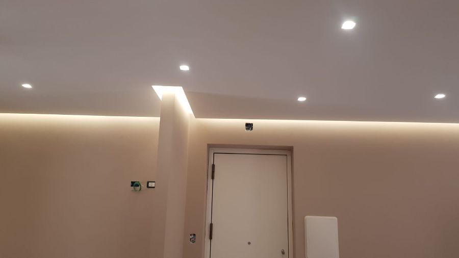 Una stanza moderna con luci da incasso e una striscia luminosa. Soffitto bianco e pareti beige, con una porta bianca.
