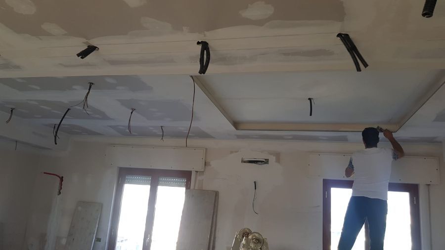 Uomo che installa le modanature del soffitto in una stanza con fili scoperti.