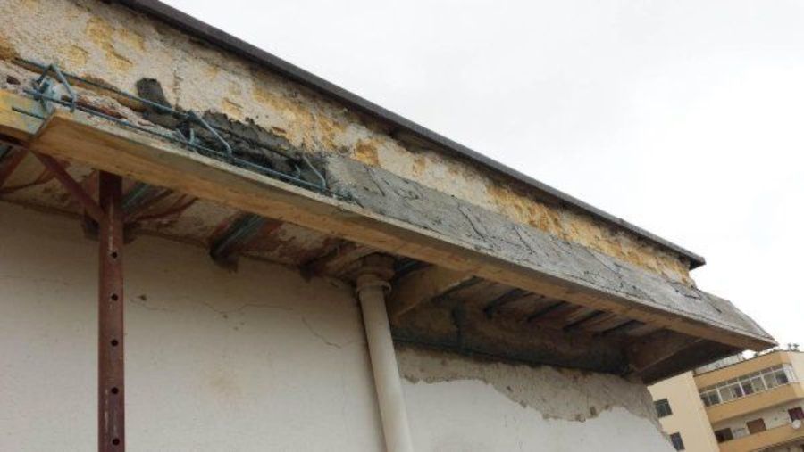 Esterno dell'edificio con struttura visibile: impalcature, assi di legno ed elementi strutturali a vista. Cielo nuvoloso.