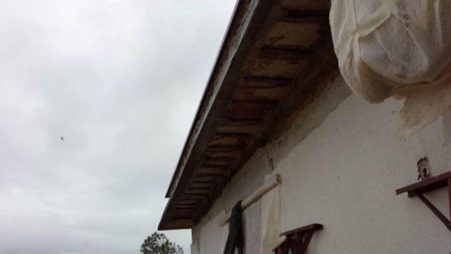 Vista laterale di un edificio con il tetto danneggiato e di una persona in piedi vicino al muro in una giornata nuvolosa.