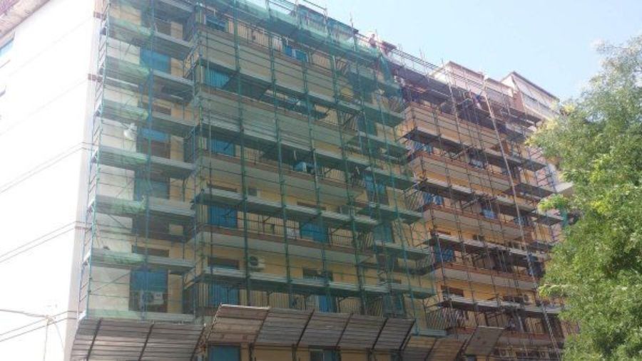 Edificio in costruzione, coperto da impalcature e reti di sicurezza, con alcune impalcature esposte.
