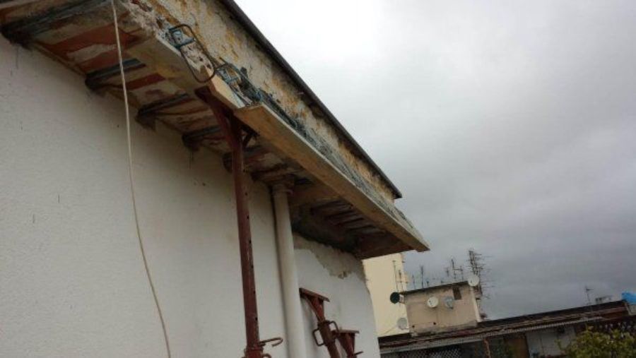 Tetto dell'edificio danneggiato con travi di sostegno al loro posto, cielo coperto.