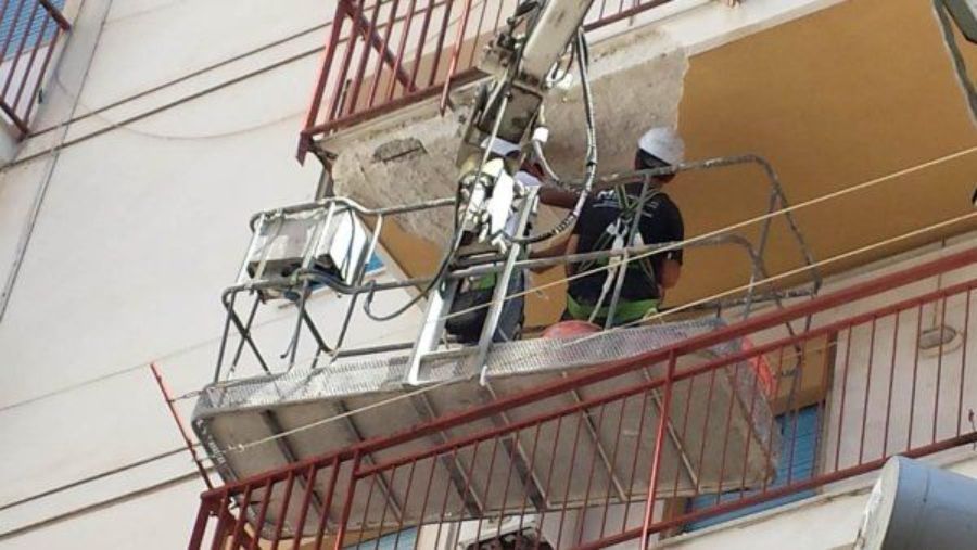 Operai in un cestello elevatore riparano danni esterni a un edificio vicino a un balcone. Caschi bianchi, esterno dell'edificio.