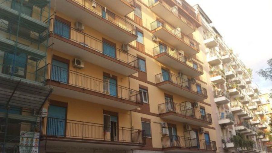 Edificio residenziale con facciata gialla, numerosi balconi e infissi blu.