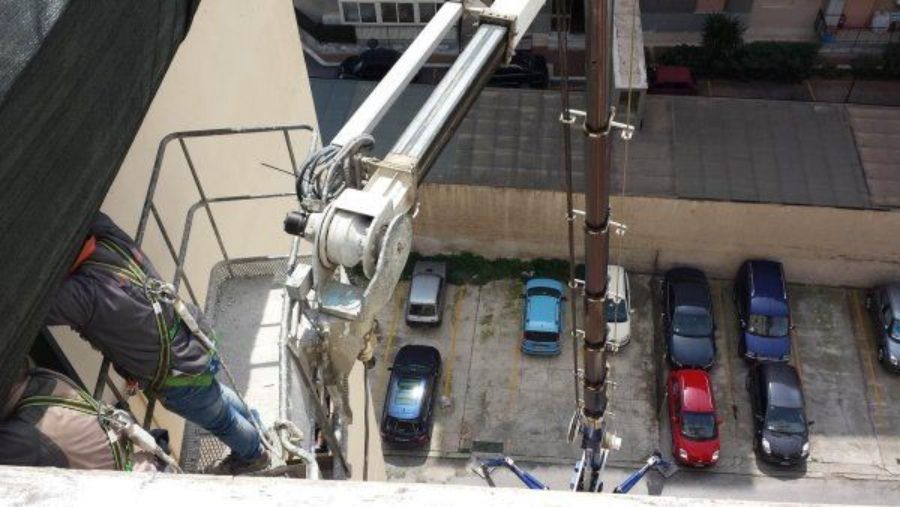 Operaio su un ascensore; braccio idraulico sopra un parcheggio con auto.