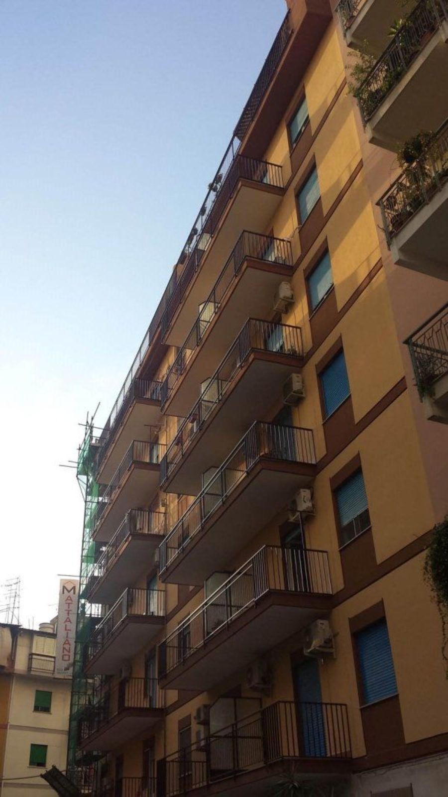 Condominio giallo con numerosi balconi che si staglia contro il cielo azzurro.