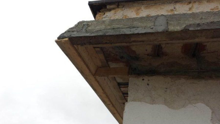 Angolo del tetto di un edificio con travi di sostegno in legno, cemento e stucco usurati.