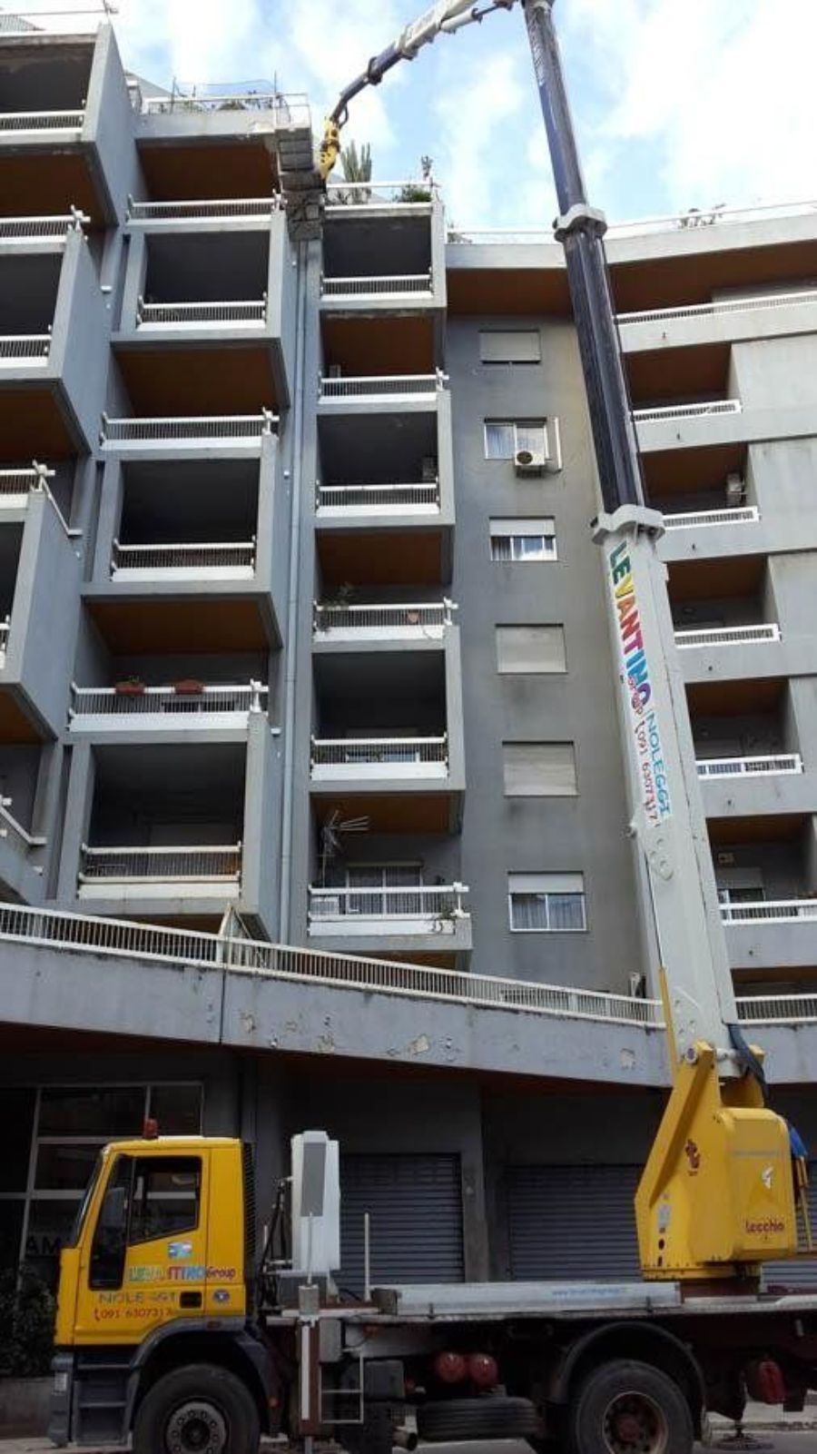 Un camion giallo con una gru che solleva detriti da un edificio a più piani.
