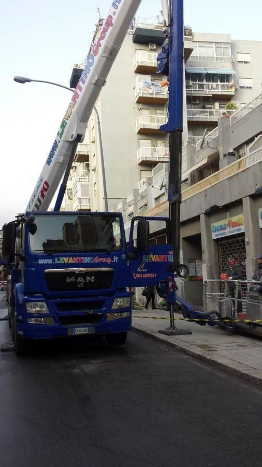 Camion blu con gru estesa in una strada cittadina, probabilmente per traslochi.