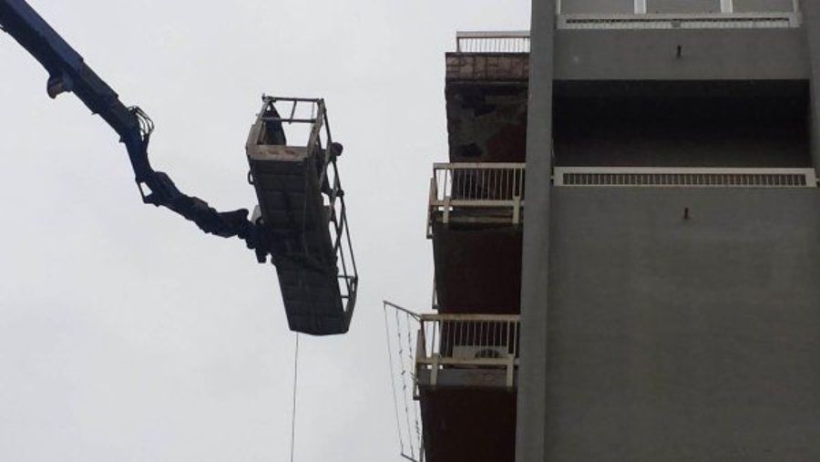 Una gru solleva una piattaforma di costruzione accanto a un edificio.